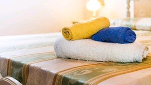 Ein Bett mit gestreifter Bettdecke und drei zusammengerollte Handtücher in Gelb, Blau und Weiß.