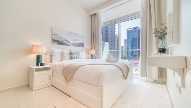 Una camera da letto moderna con un letto grande, comodini, un tavolino e una finestra con tende, con vista sugli edifici.