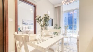 Zona pranzo con tavolo bianco apparecchiata per quattro persone, un vaso con fiori e vista sulla città attraverso ampie finestre.