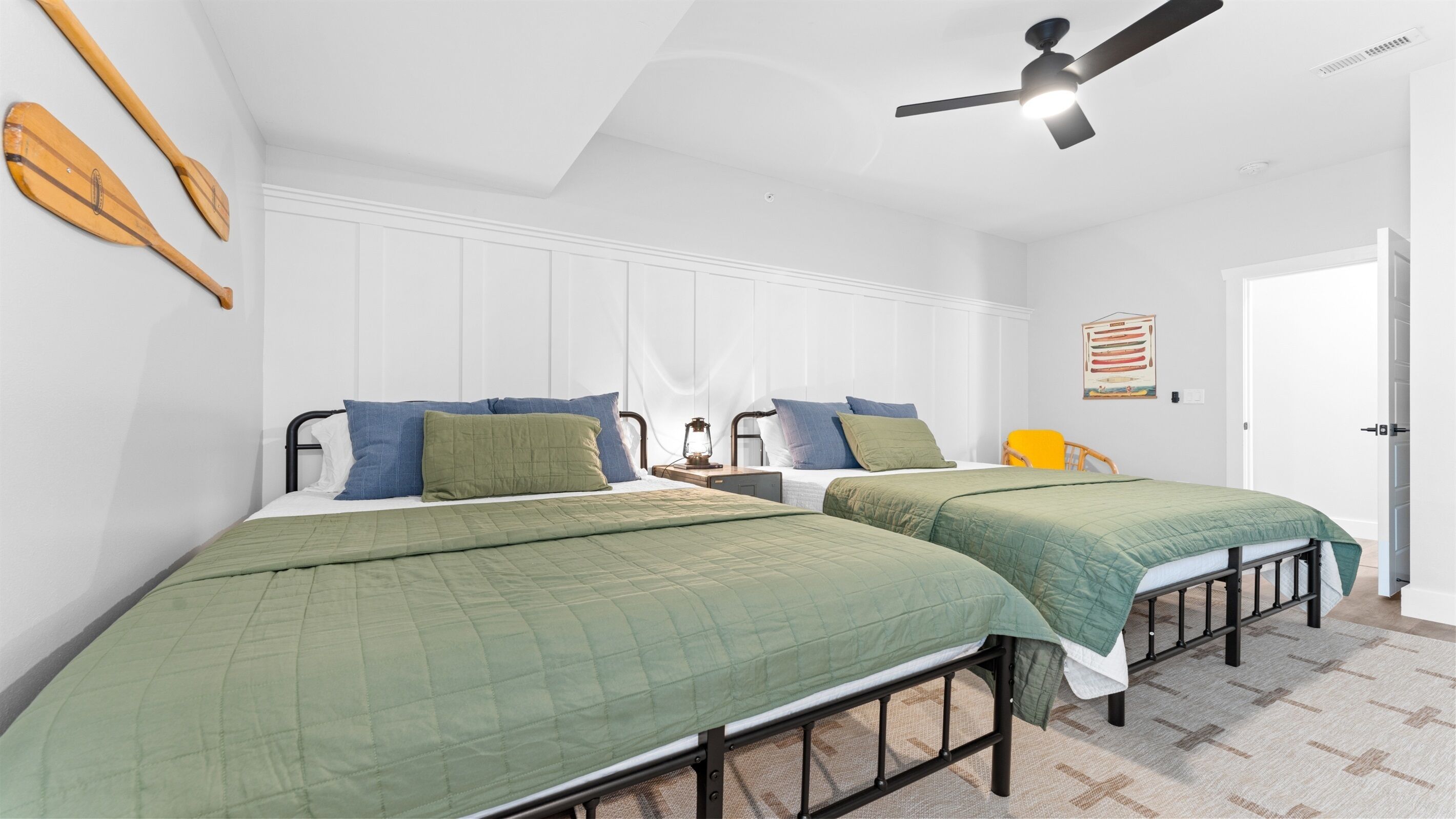 Quarto com duas camas, um ventilador de teto e uma luminária na parede.