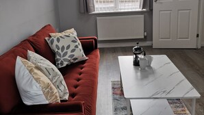 A modern living room with a red sofa, a white coffee table, and a window with curtains. - Olive and Carol's Beautiful 3-bed House in Walsall (Walsall)