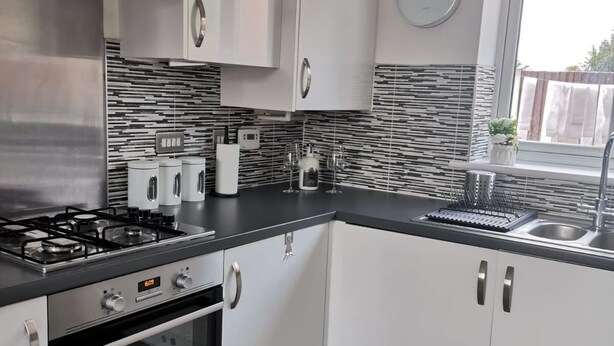 A modern kitchen with white cabinets, a stainless steel range hood, a built-in oven, and a black countertop. - Olive and Carol's Beautiful 3-bed House in Walsall (Walsall)