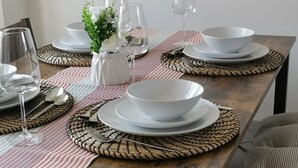 A dining table set with white plates, bowls, and glasses, accompanied by woven placemats and a vase with white flowers. - Olive and Carol's Beautiful 3-bed House in Walsall (Walsall)
