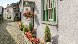 A narrow cobblestone street lined with traditional buildings, each with a sign indicating their former names. - Leafy Nook Lodge (Ambleside)