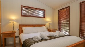 A neatly made bed with white linens, two bedside tables with lamps, and wooden blinds on the windows. - Leafy Nook Lodge (Ambleside)