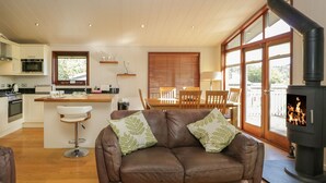 A cozy living room with a brown leather sofa, a wooden dining table, and a kitchen area with a stove and microwave. - Leafy Nook Lodge (Ambleside)