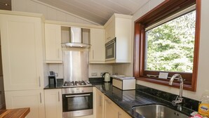A modern kitchen with white cabinets, a stainless steel stove, and a window with a view of greenery. - Leafy Nook Lodge (Ambleside)