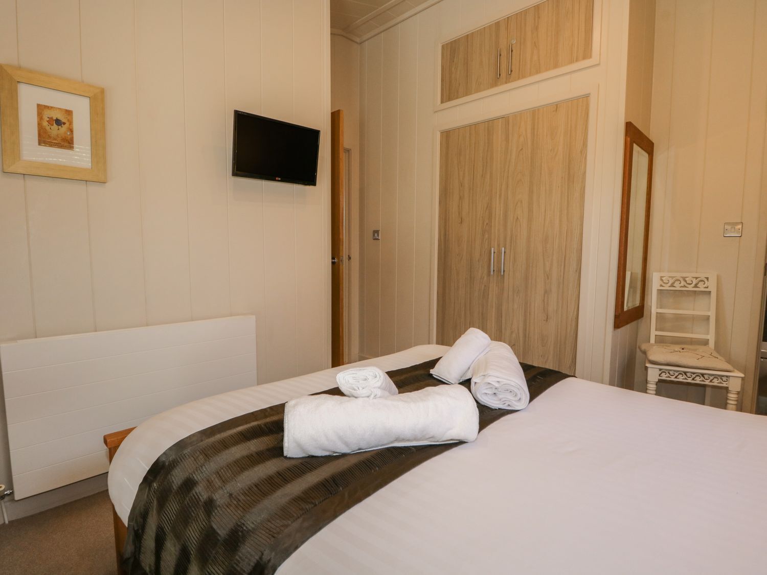 Une chambre d’hôtel comprenant un lit, une télévision, une armoire et une petite table avec une chaise.