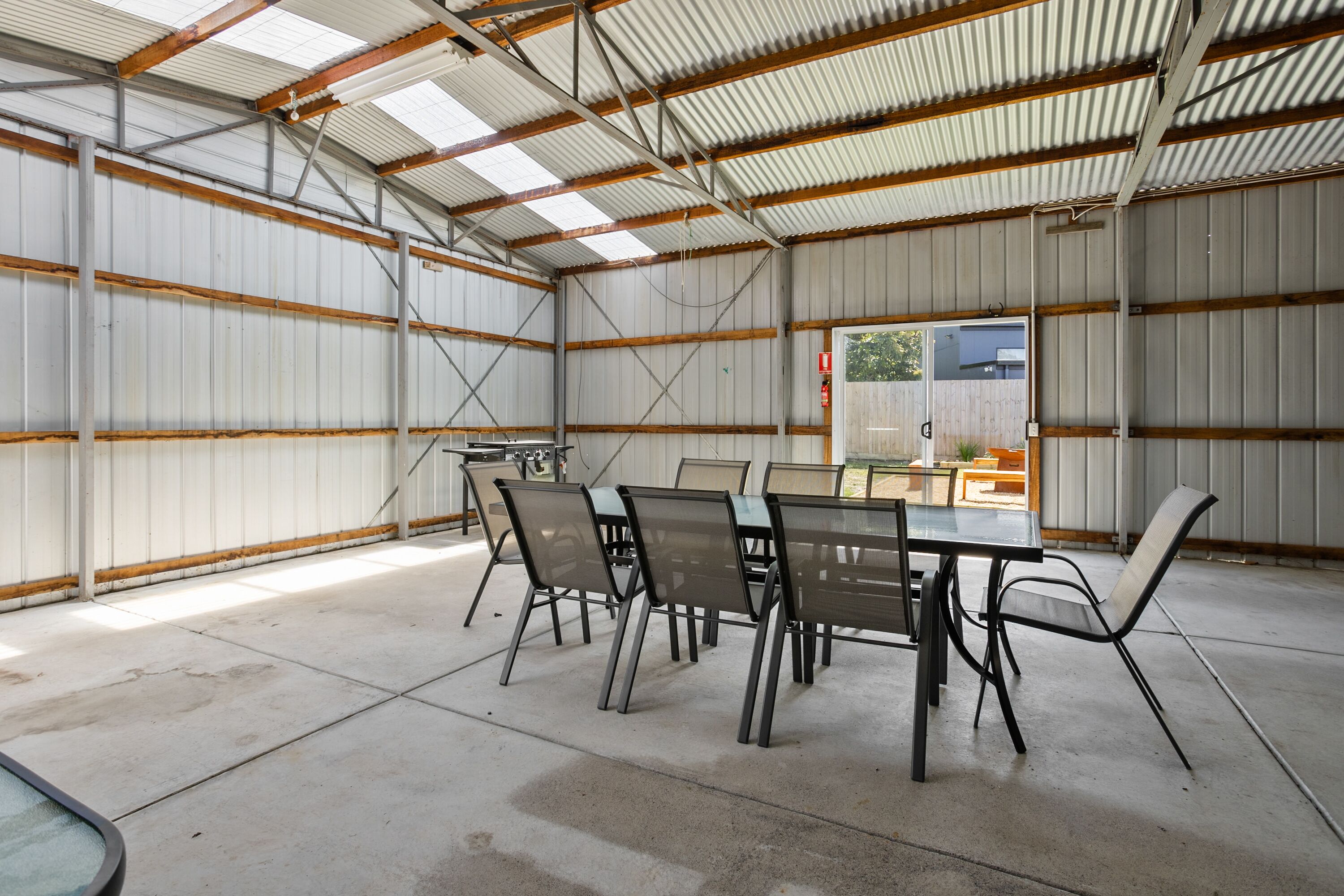 A spacious indoor area with a long table and chairs, high ceilings with metal beams, and a view of the outside.