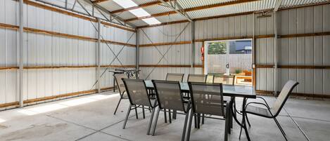 A spacious indoor area with a long table and chairs, high ceilings with metal beams, and a view of the outside.