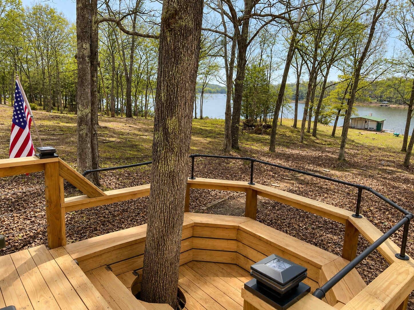 Eine Holzterrasse mit Geländer, einer Flagge und Blick auf einen von Bäumen umgebenen See.