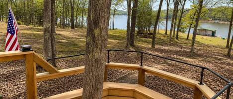 A wooden deck with a railing, a flag, and a view of a lake surrounded by trees.