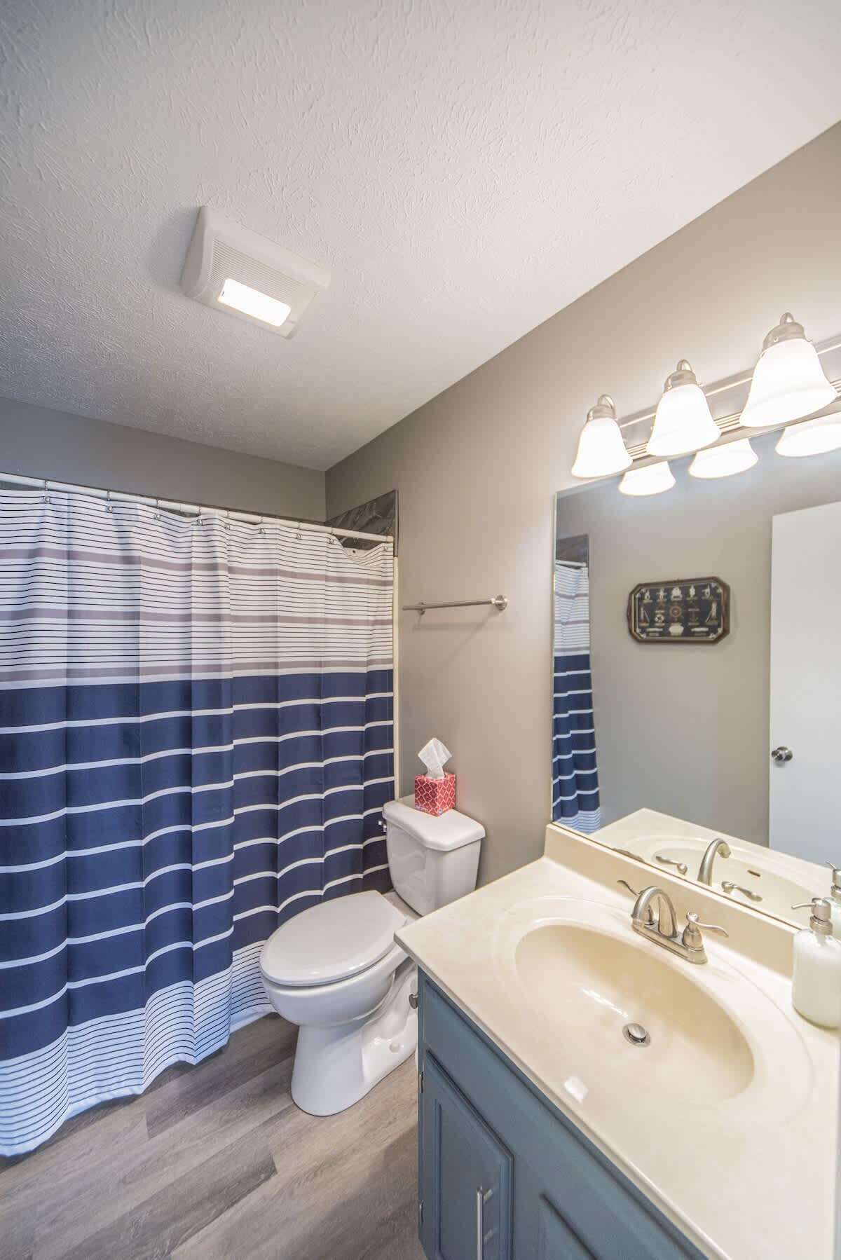 Une salle de bain avec un rideau de douche à rayures, des toilettes, un lavabo avec un miroir et un porte-serviettes.