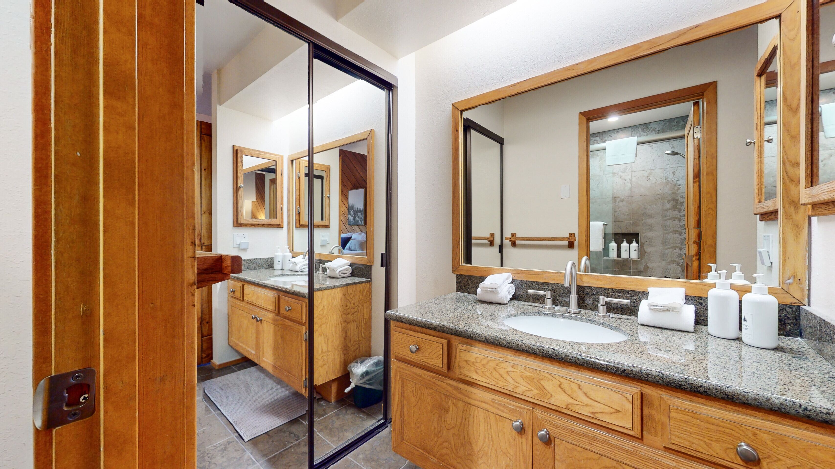 A modern bathroom with a wooden vanity, a large mirror, and a granite countertop.
