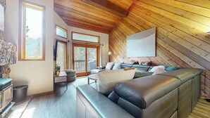 A cozy living room with a wooden ceiling, a large sofa, a dining table, and a view through the windows. - Pet-Friendly, Renovated, Spacious, Great Lighting. Private Gas Grill, Laundry (Mammoth Lakes)