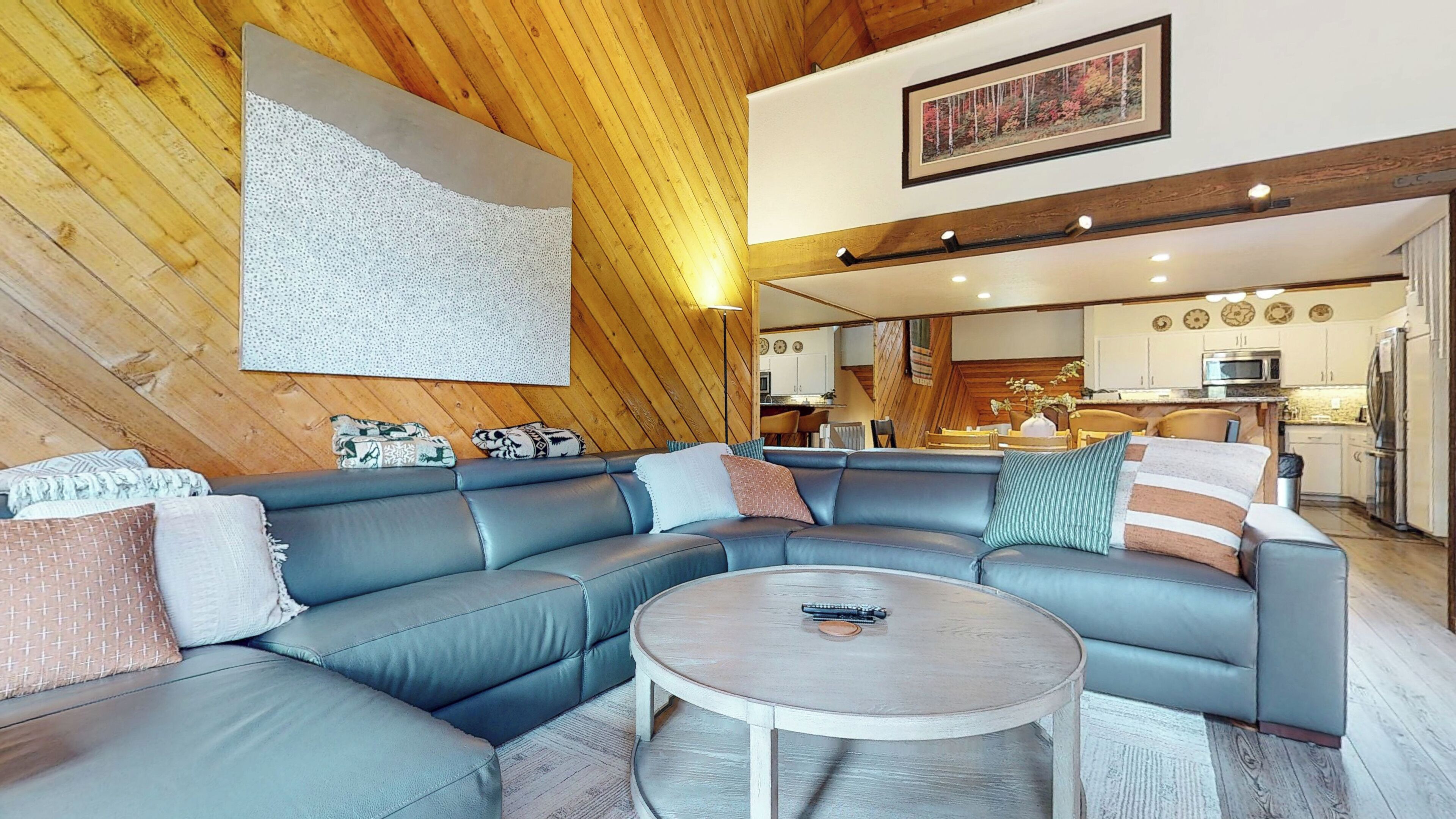 A modern living room with a sectional sofa, a round coffee table, and a wooden ceiling.