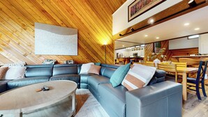 A modern living room with a sectional sofa, a round coffee table, and a dining area with wooden chairs and a table. - Pet-Friendly, Renovated, Spacious, Great Lighting. Private Gas Grill, Laundry (Mammoth Lakes)