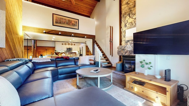 A modern living room with a sectional sofa, a coffee table, and a TV. There is a kitchen in the background with a microwave and a dining area. - Pet-Friendly, Renovated, Spacious, Great Lighting. Private Gas Grill, Laundry (Mammoth Lakes)
