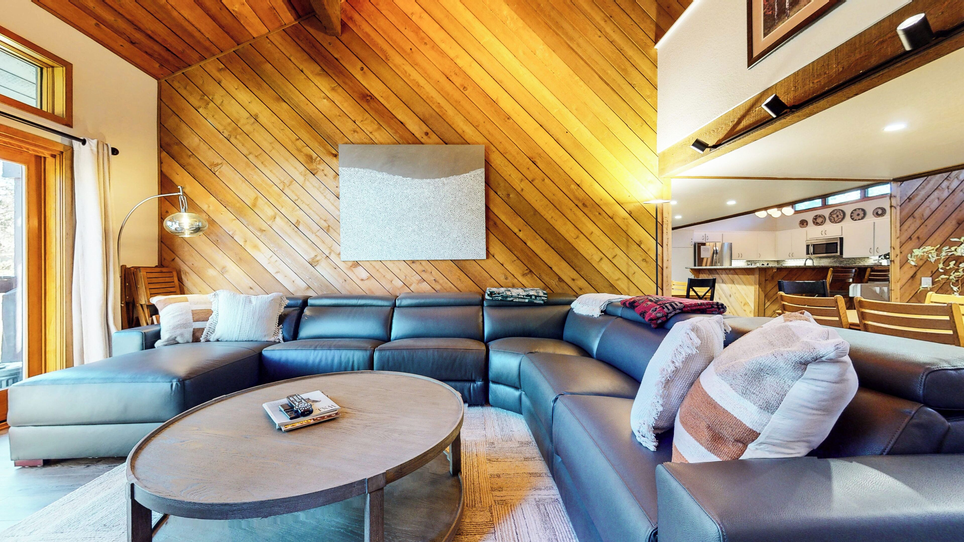 A modern living room with a large L-shaped sectional sofa, a round coffee table, and a kitchen area visible in the background.