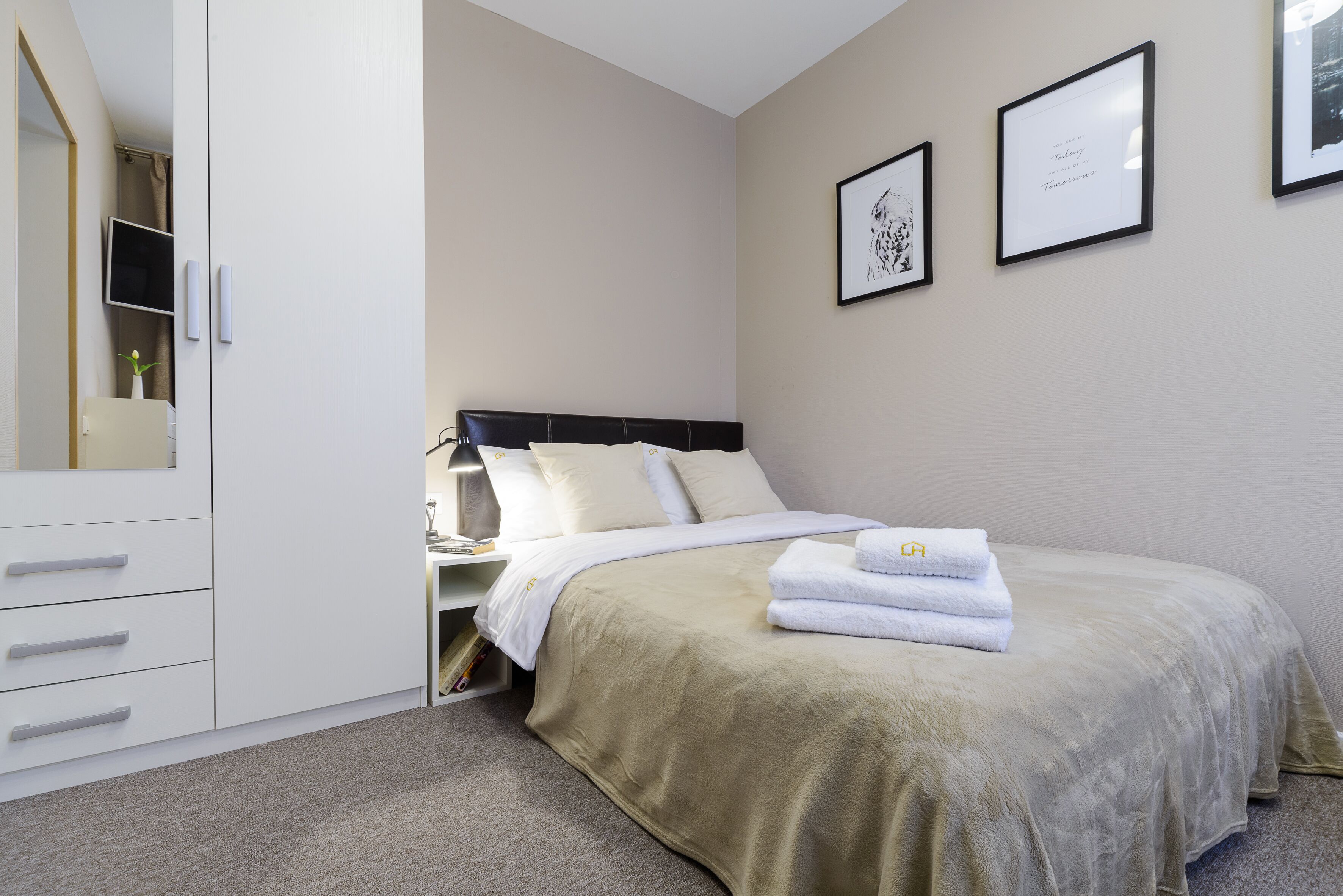 A neatly arranged bedroom with a bed, a wardrobe, and a nightstand.