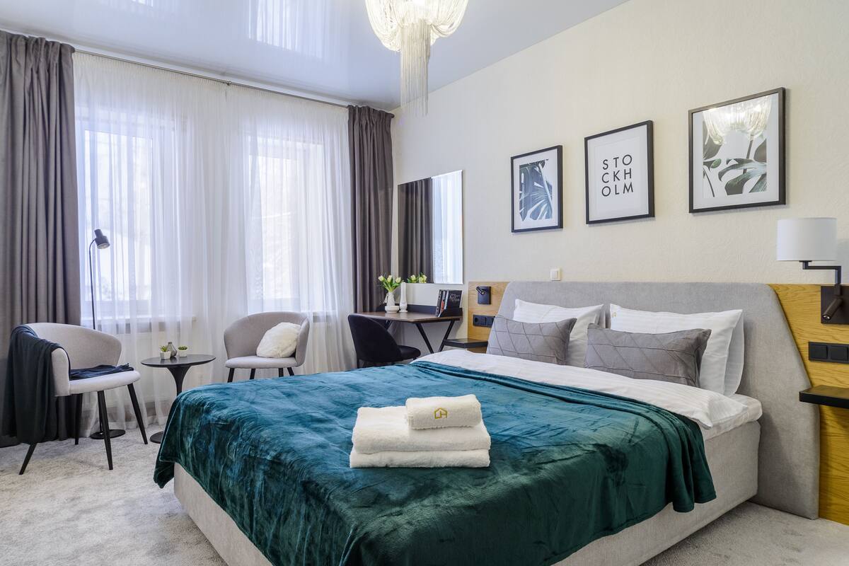 A hotel room with a bed, two chairs, a desk, and a large window with curtains.