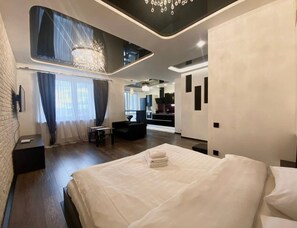 A modern hotel room with a large bed, a desk, a chair, and a view of the kitchen area. - HomeApart Novgorodskaya street (Minsk)