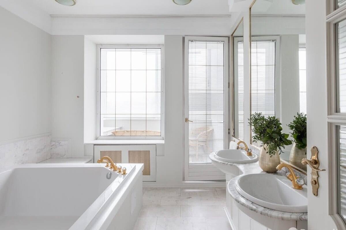 A modern bathroom with a bathtub, two sinks, and a large window.