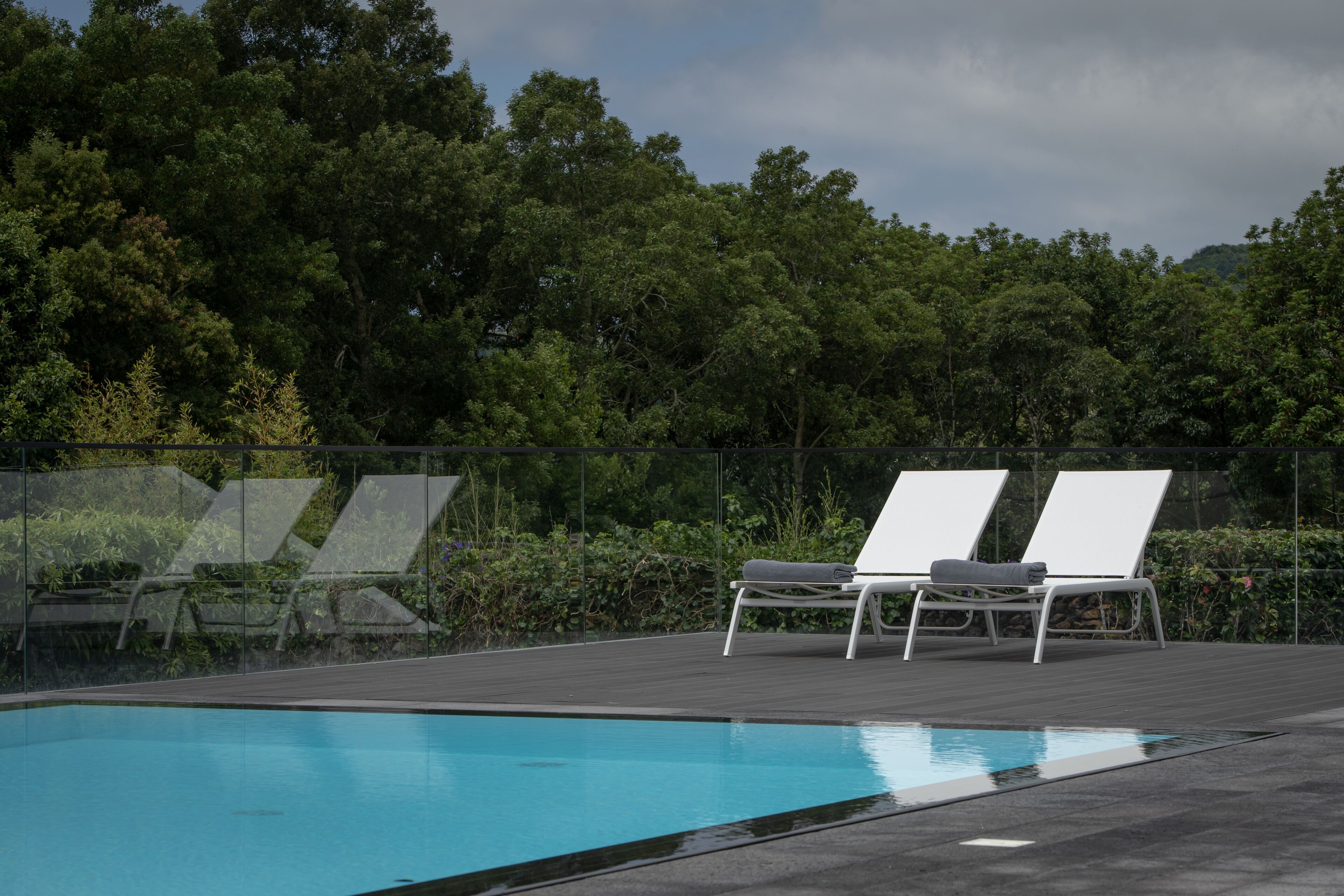 A swimming pool with two white lounge chairs and a glass barrier.