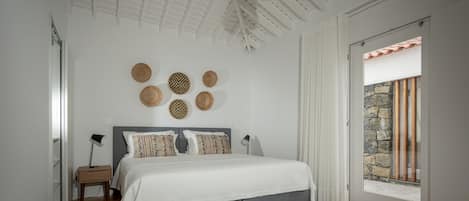 Un dormitorio con cama, mesitas de noche, una lámpara de pared y vistas a través de un ventanal.