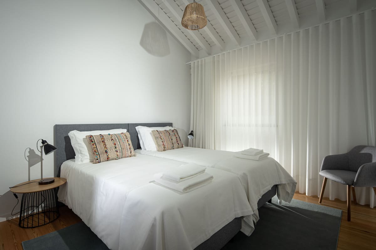 Quarto de hotel bem arrumado com uma cama grande, uma cadeira, uma escrivaninha e um abajur.