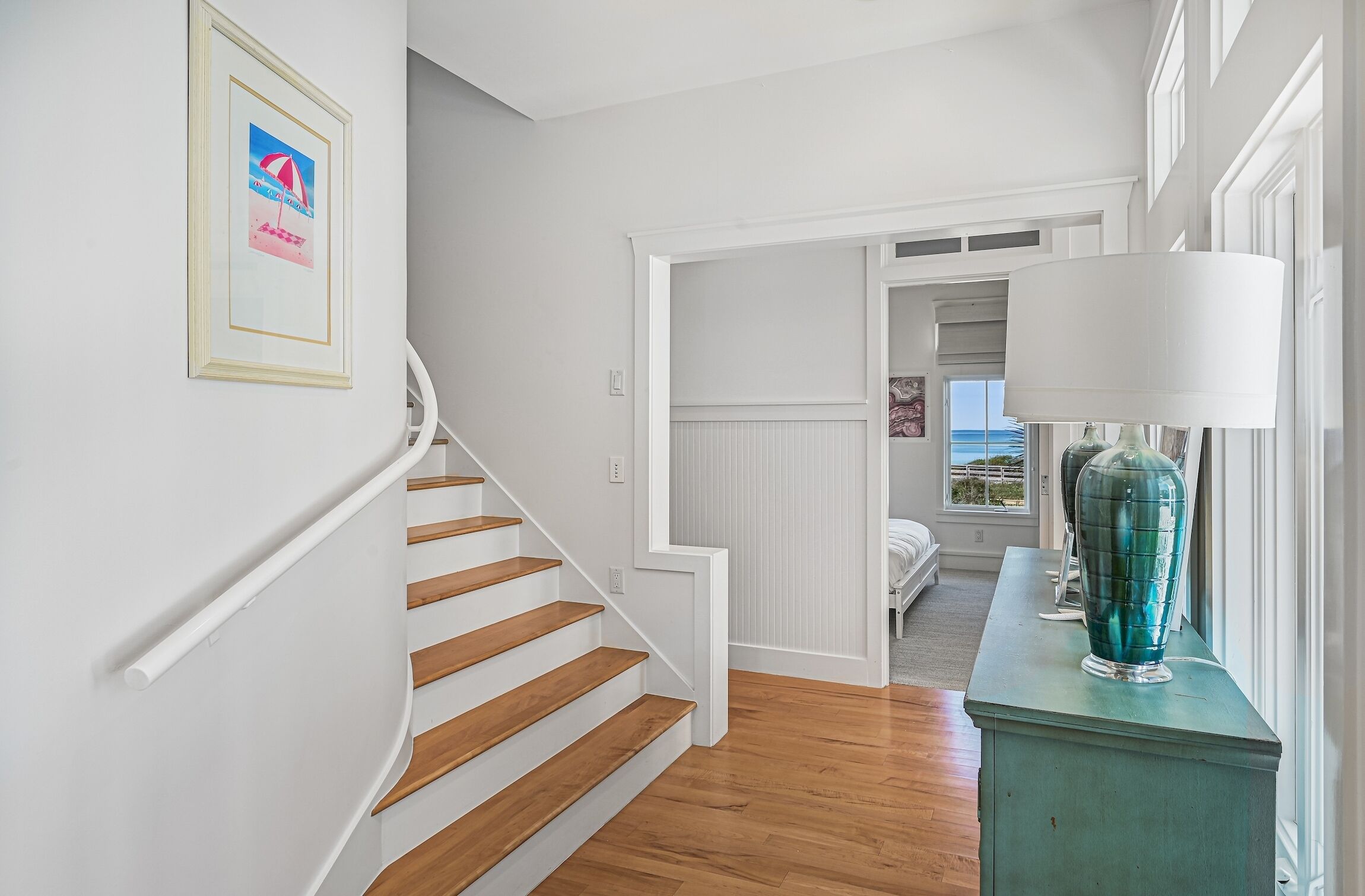 A staircase with wooden steps and white walls, leading to a room with a view of the ocean.