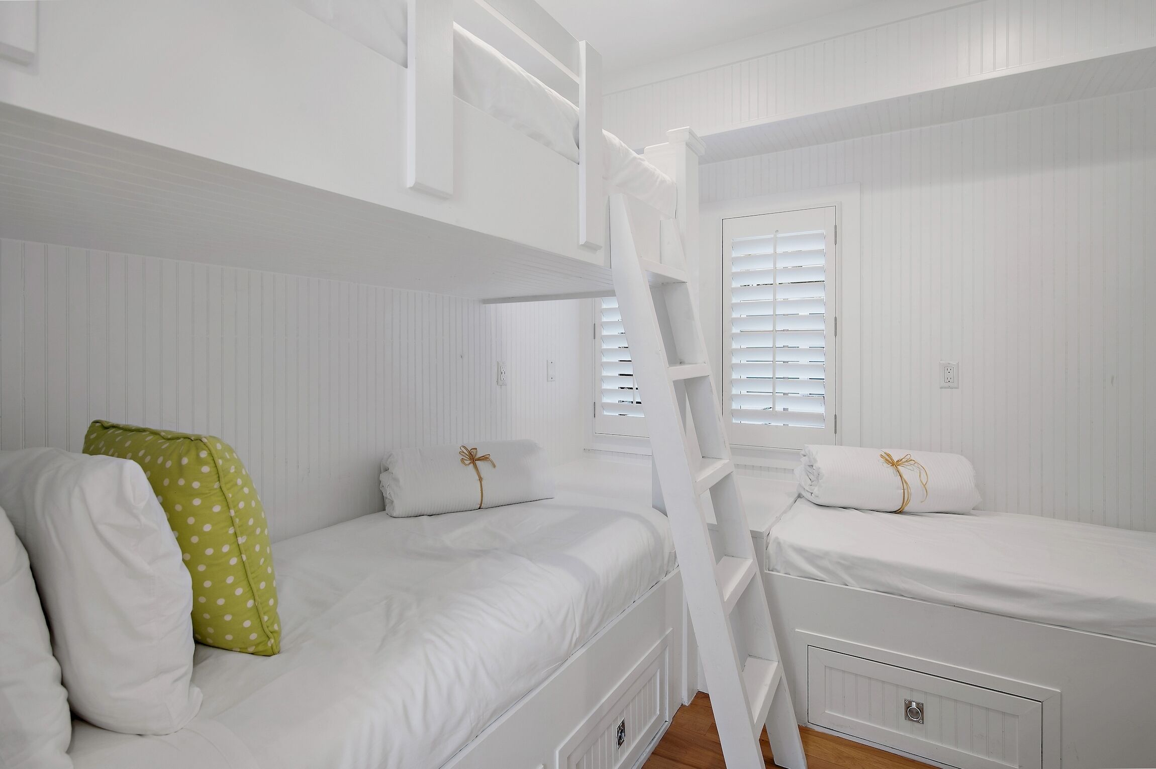 A bunk bed room with white bedding and a ladder.