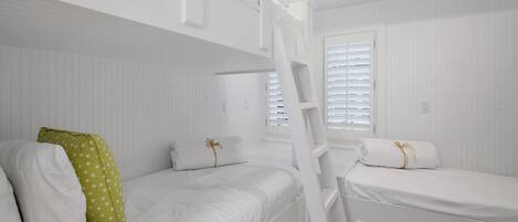 A bunk bed room with white bedding and a ladder.