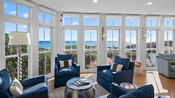 A spacious living room with large windows, a view of the ocean, and blue furniture.