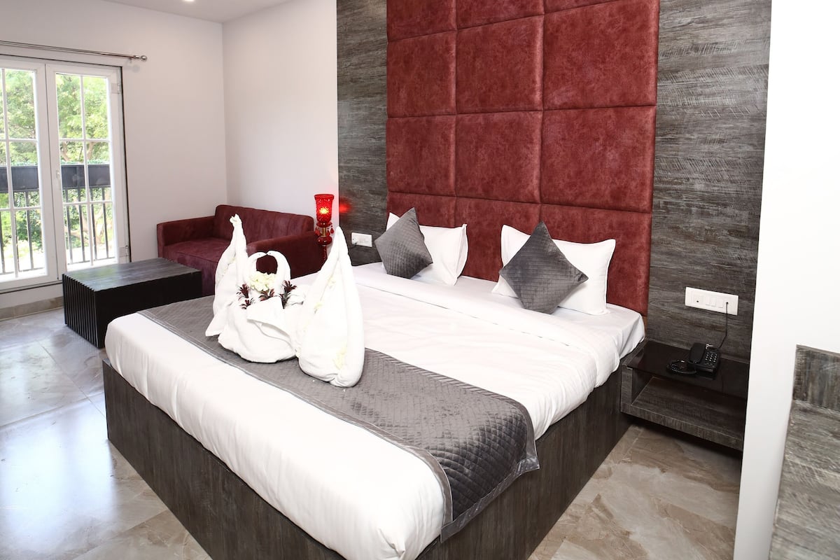 A modern hotel room with a large bed, a red accent wall, a ceiling fan, and a view of the outdoors.