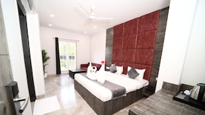 A modern hotel room with a large bed, a red accent wall, a ceiling fan, and a small table with a kettle. - Hotel Thor (Agra)