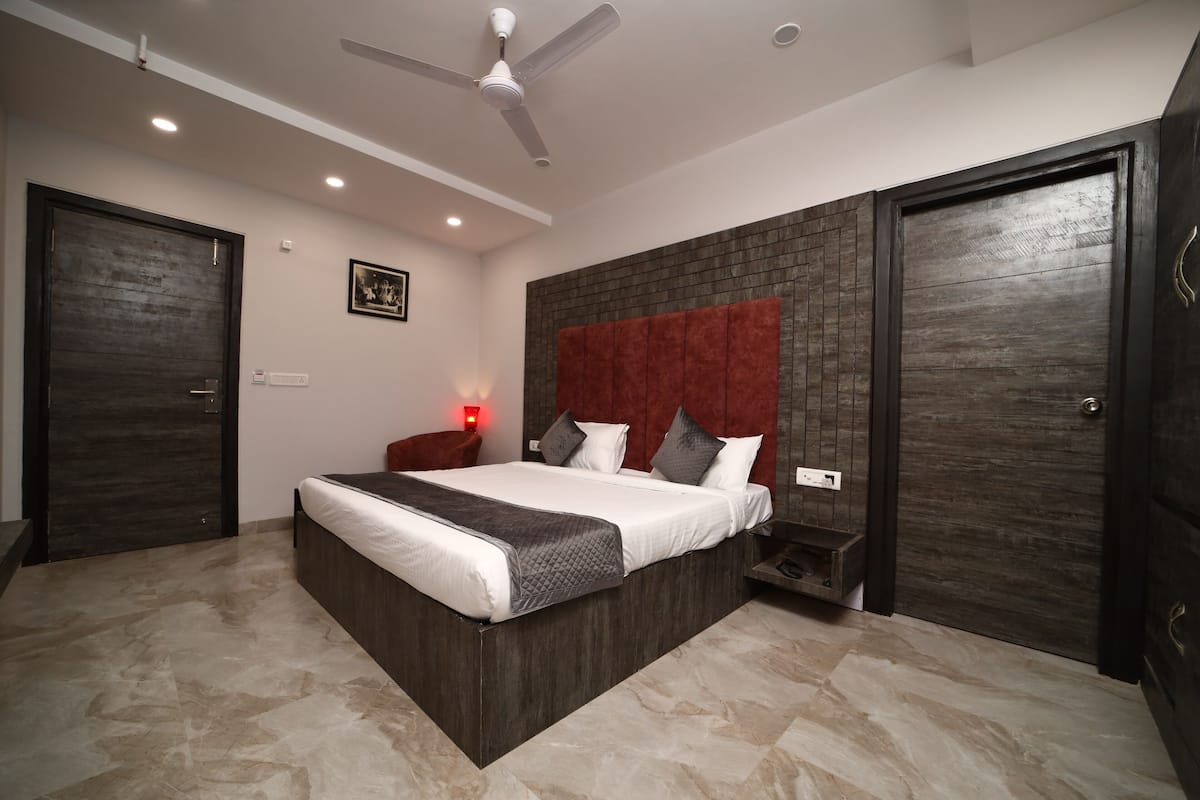 A modern bedroom with a large bed, dark wood paneling, a ceiling fan, and a red accent wall.