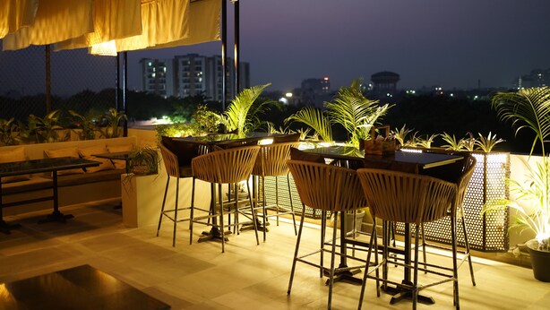 An outdoor seating area with a table and chairs, surrounded by potted plants and a view of the city skyline at night. - Hotel Thor (Agra)