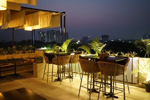 Een terras met een tafel en stoelen, omringd door potplanten en uitzicht op de skyline van de stad 's nachts.