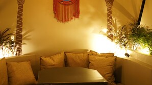 A cozy room with a curved sofa, a small table, and a wall decorated with palm tree designs and a mirror. - Hotel Thor (Agra)