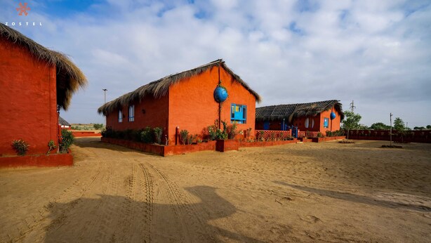 A rural setting with thatched-roof buildings, a dirt path, and a clear sky. - Zostel Sam Desert (Jaisalmer) (Jaisalmer)