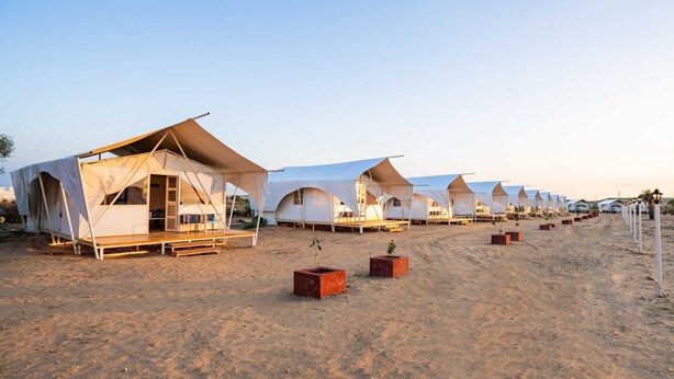 Une rangée de tentes blanches à toit plat, disposées sur une plage de sable.