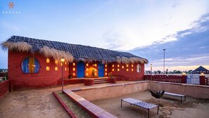 Un bâtiment rouge avec un toit de chaume, des panneaux solaires et une cour intérieure dotée de bancs et de plantes en pot.
