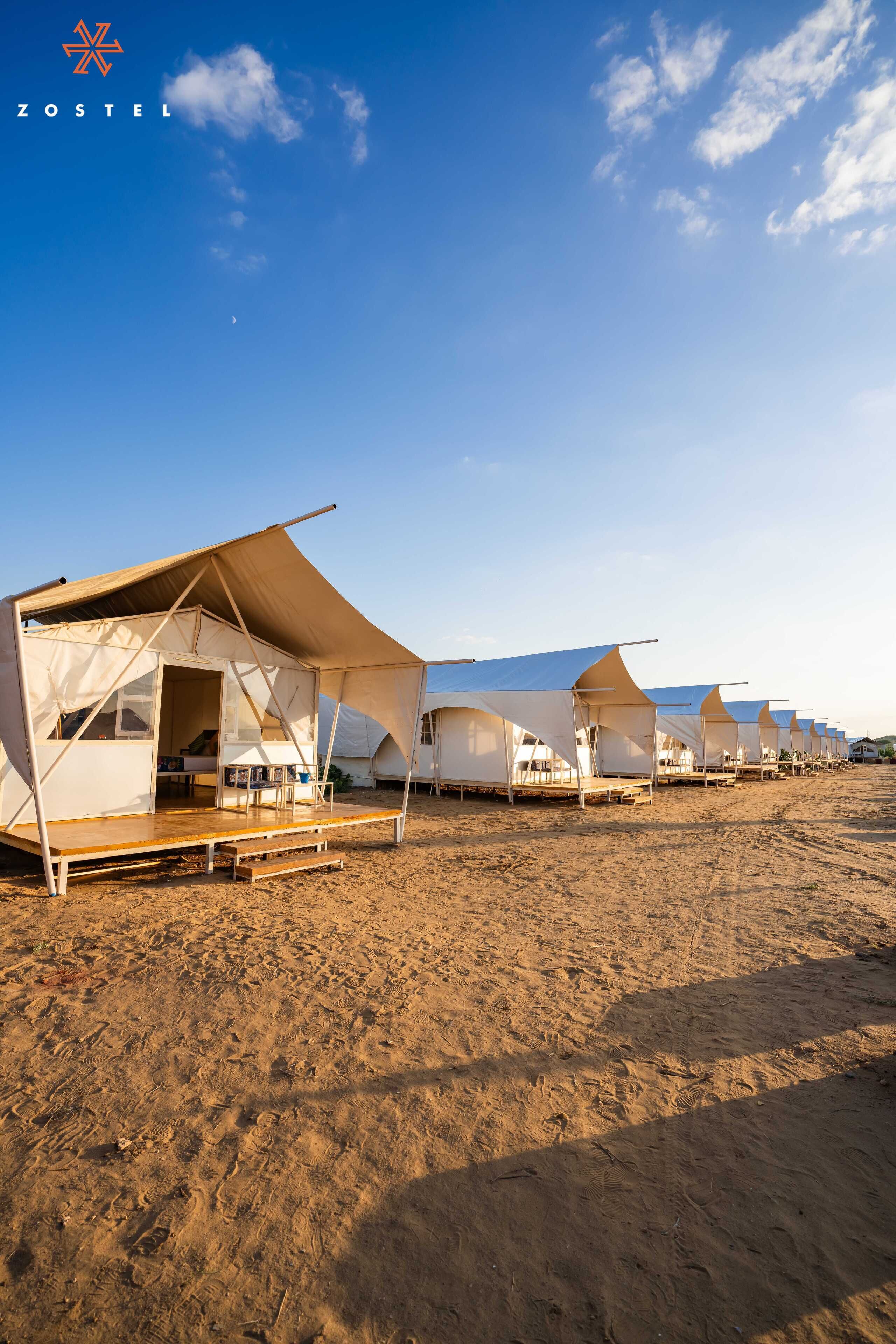 A row of white tents with a flat roof, arranged on a sandy beach.