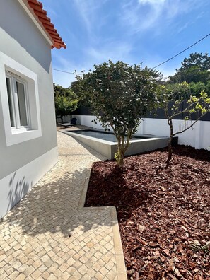 Zona residencial con un camino pavimentado, un árbol y un edificio blanco con techo rojo.