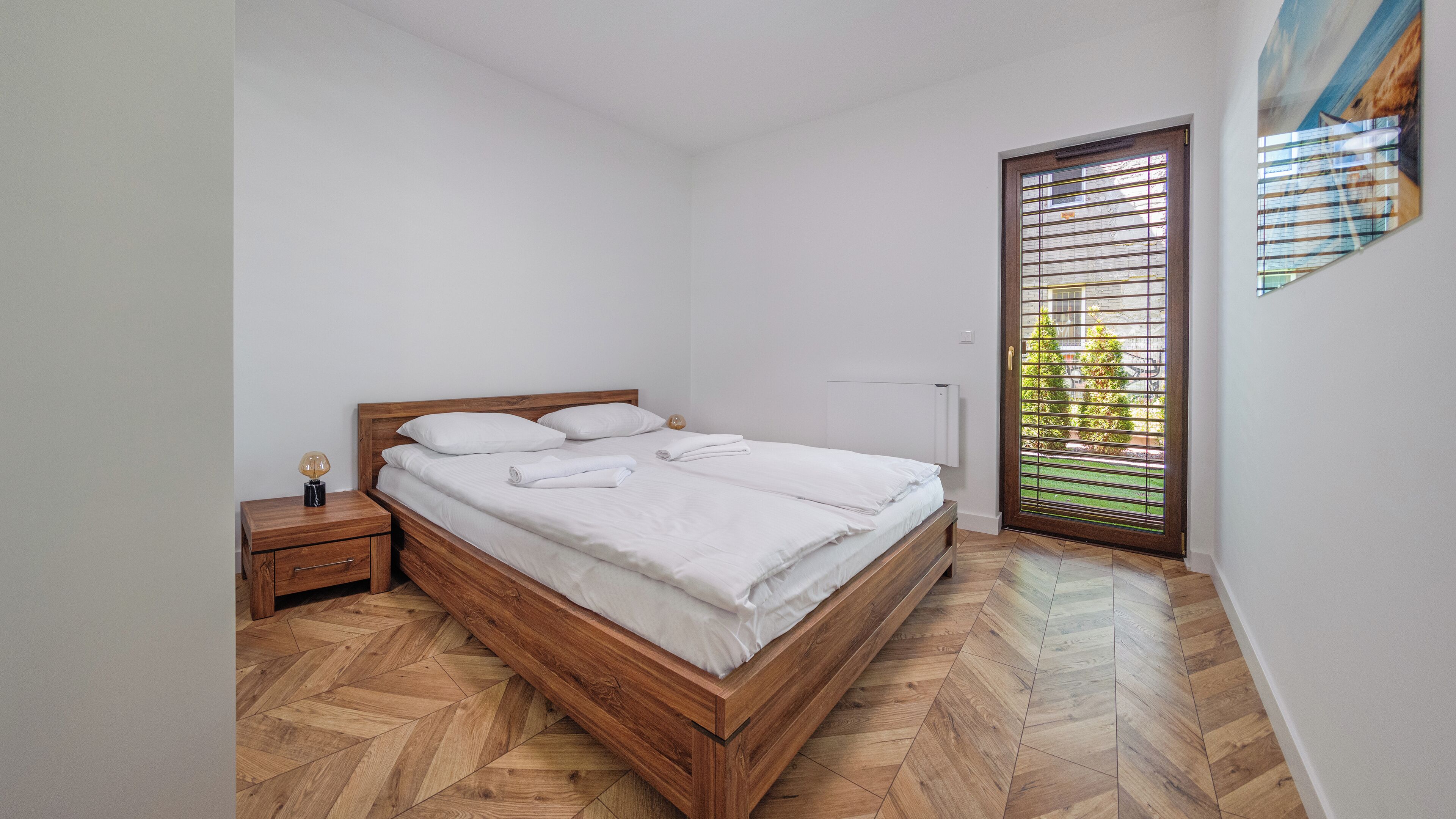 Ein Schlafzimmer mit einem hölzernen Bett, einem Nachttisch, einer Lampe und einem Fenster mit Jalousien.