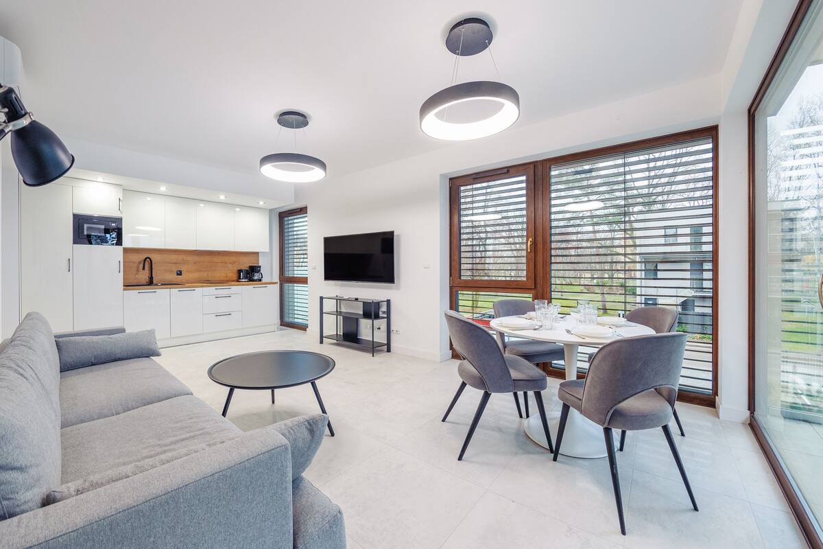 A modern kitchen with white cabinets, a wooden countertop, and a flat-screen TV. There is a dining area with a round table and four chairs.
