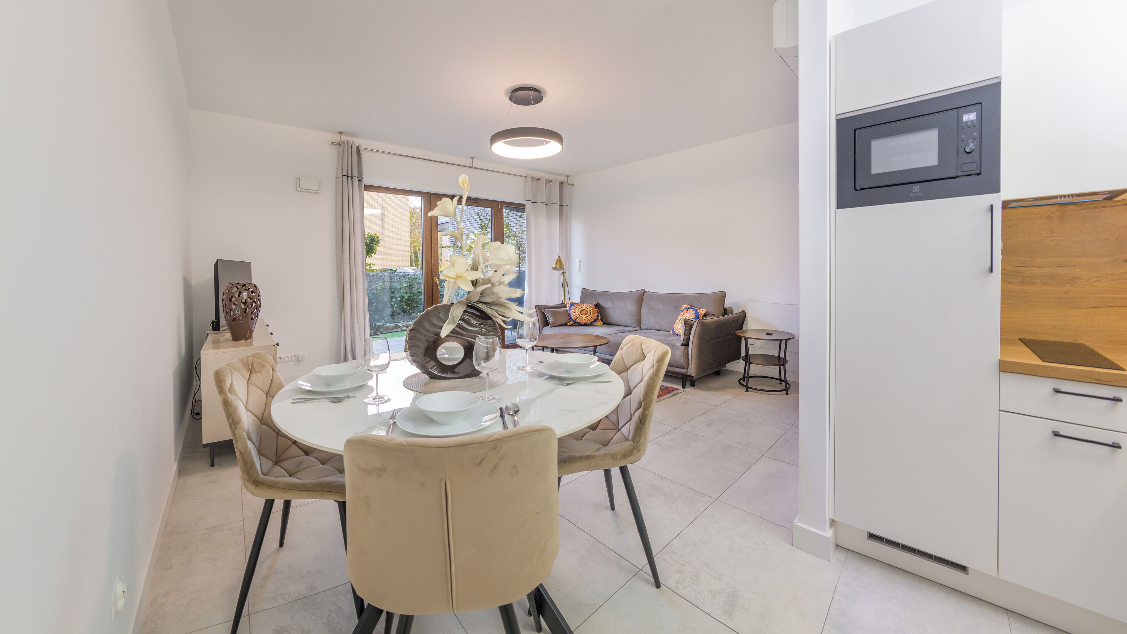 Un espace repas moderne avec une table ronde pour quatre personnes, un canapé et un coin cuisine équipé d’un four à micro-ondes.