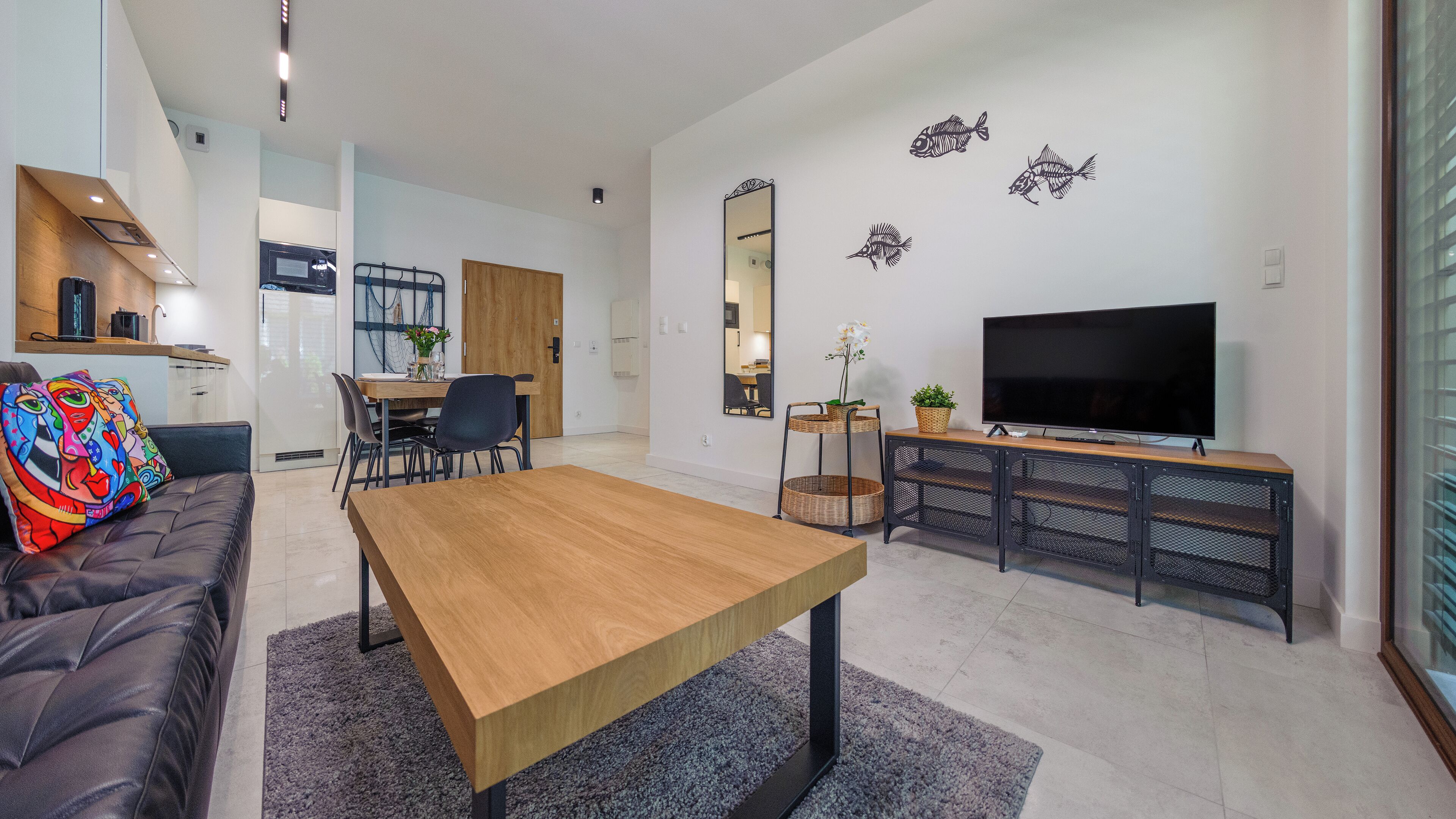 A modern living room with a wooden dining table, a sofa, a TV, and decorative fish wall art.