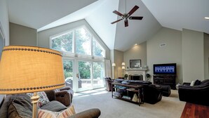 A spacious living room with a large window, a ceiling fan, a fireplace, and a television. - 17 Cartgate - Palmetto Dunes - 4 Bed 4 Bath Private Pool -Hilton Head Rentals (Hilton Head Island)